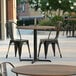 A Lancaster Table & Seating Excalibur round table with a textured wood table top on a patio with chairs.