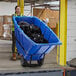 A woman in a yellow vest pushing a Lavex blue tilt truck full of black garbage bags.