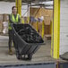 A woman pushing a black Lavex Heavy-Duty Tilt Truck full of garbage.