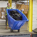 A woman in a yellow vest pushing a blue Lavex trash cart full of garbage.