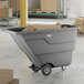 A gray Lavex tilt truck or trash cart with a 1 cubic yard capacity, holding cardboard boxes in a warehouse setting.