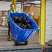 A woman pushing a blue Lavex tilt truck full of black garbage bags.