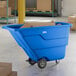 A blue Lavex 1 cubic yard tilt truck or trash cart with a 600 lb. capacity, shown in a warehouse setting with cardboard boxes inside.