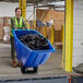 A woman in a safety vest pushing a Lavex blue tilt truck full of black garbage bags.