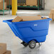 A blue Lavex tilt truck or trash cart with a 0.5 cubic yard capacity, holding cardboard boxes in a warehouse setting.
