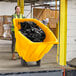 A woman in a yellow vest pushing a yellow Lavex tilt truck full of black plastic bags.