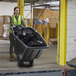 A woman in a green vest pushing a Lavex black garbage cart.