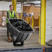 A woman in a safety vest pushing a Lavex black tilt truck full of garbage.