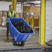 A woman in a safety vest pushing a blue Lavex tilt truck full of black garbage bags.