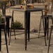 A Lancaster Table & Seating distressed copper bar height table on an outdoor patio.