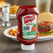 A French's Tomato Ketchup bottle on a table next to a plate of food with a hamburger.
