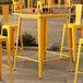 A Lancaster Table & Seating yellow metal table on an outdoor stone patio.