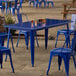 A blue Lancaster Table & Seating outdoor table on a stone surface with blue chairs.