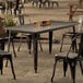A Lancaster Table & Seating Alloy Series distressed onyx black table and chairs on an outdoor patio.