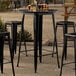 A Lancaster Table & Seating black metal bar height table with black chair legs.