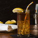 A glass of iced tea with a yellow and white striped Aardvark Eco-Flex paper straw and a lemon wedge.