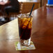 A glass of brown liquid with ice and a black Aardvark jumbo paper straw in it.