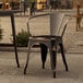 A Lancaster Table & Seating Distressed Copper outdoor arm chair on a stone patio.