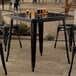 A Lancaster Table & Seating Onyx Black metal table with chairs on an outdoor patio.