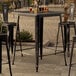 A Lancaster Table & Seating distressed onyx black bar table with drinks on it and chairs on a patio.