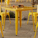 A Lancaster Table & Seating citrine yellow metal table with chairs on a patio.