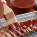 A hand using a paint brush to apply Cattlemen's Kentucky Bourbon BBQ Sauce to a rack of ribs.