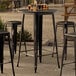 A Lancaster Table & Seating round black bar table with a distressed finish.