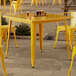 A Lancaster Table & Seating yellow table with chairs on a patio.