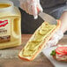 A person spreading French's Spicy Brown Mustard on a sandwich.