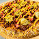 A cheeseburger-inspired pizza topped with ground beef, pickles, diced tomatoes, cheddar cheese, and drizzled with yellow mustard on a sesame seed crust.