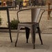 A brown Lancaster Table & Seating Alloy Series copper arm chair on a stone patio.