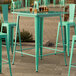 A Lancaster Table & Seating aquamarine outdoor table with two green chairs.