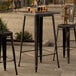 A Lancaster Table & Seating distressed copper bar height table on a stone patio.