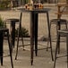 A Lancaster Table & Seating Alloy Series distressed copper bar height outdoor table with a group of stools on a patio.