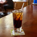 A close-up of a glass of brown liquid with ice and a white Aardvark paper straw.