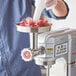 A man using the Estella meat grinder attachment to grind meat on a counter.