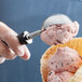 A hand using a Tablecraft FirmGrip ice cream scoop to add a scoop of ice cream to a waffle cone.