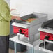 A woman in a green shirt using an Avantco Chef Series countertop gas griddle to cook food.