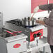 An Avantco Chef Series countertop gas range with two silver pots on burners, one with a wooden spoon in it.