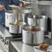 A man using a Choice aluminum sauce pot on a stove in a professional kitchen.