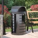 A black Suncast round metal trash can with a lid next to a bench.