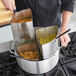 A man using a Choice perforated stainless steel strainer basket to cook pasta in a pot.