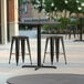 A Lancaster Table & Seating Excalibur round table with black stools on a patio.