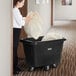 A woman using a Lavex black cube truck to put a large bag in a trash can.