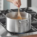 A person stirring soup in a Choice aluminum sauce pot on a stove.