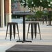 A Lancaster Table & Seating Excalibur table with black stools on a patio.