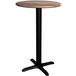 A Lancaster Table & Seating round counter height table with a wooden top and black cross base.