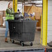 A woman in a green safety vest pushing a black Lavex cube truck.