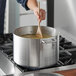 A person stirring food in a Choice aluminum sauce pot on a stove.