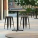 A Lancaster Table & Seating Excalibur table and stools on a patio with a cross base plate.